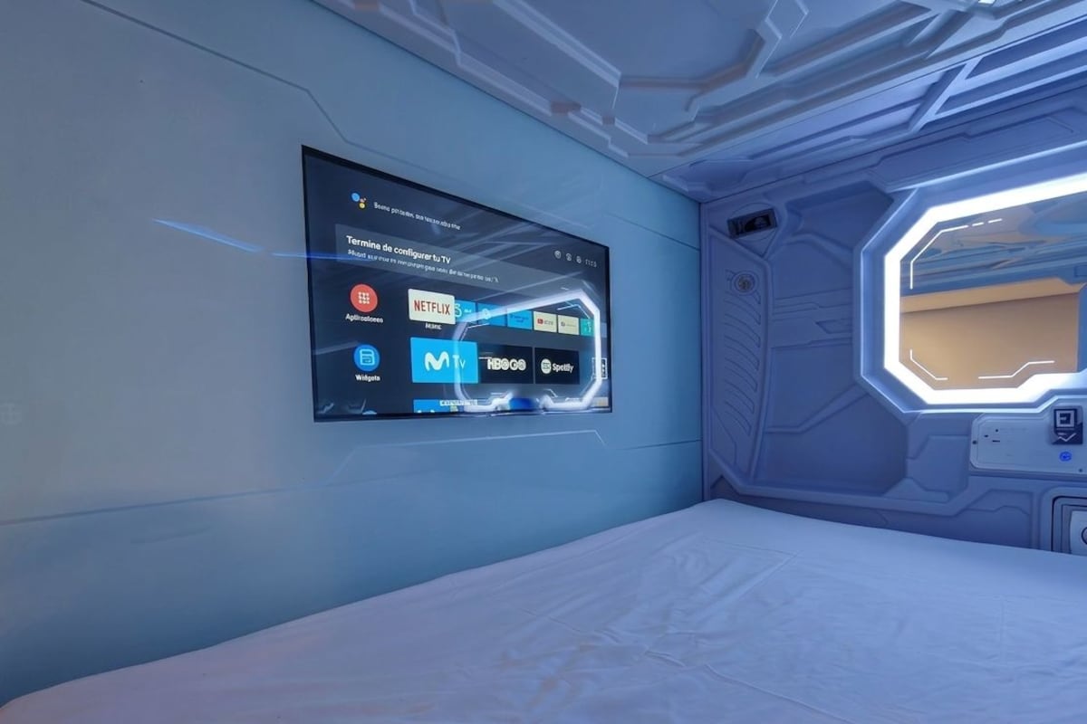 A futuristic room with a large digital display on the wall, a bed, and a window with a geometric design.