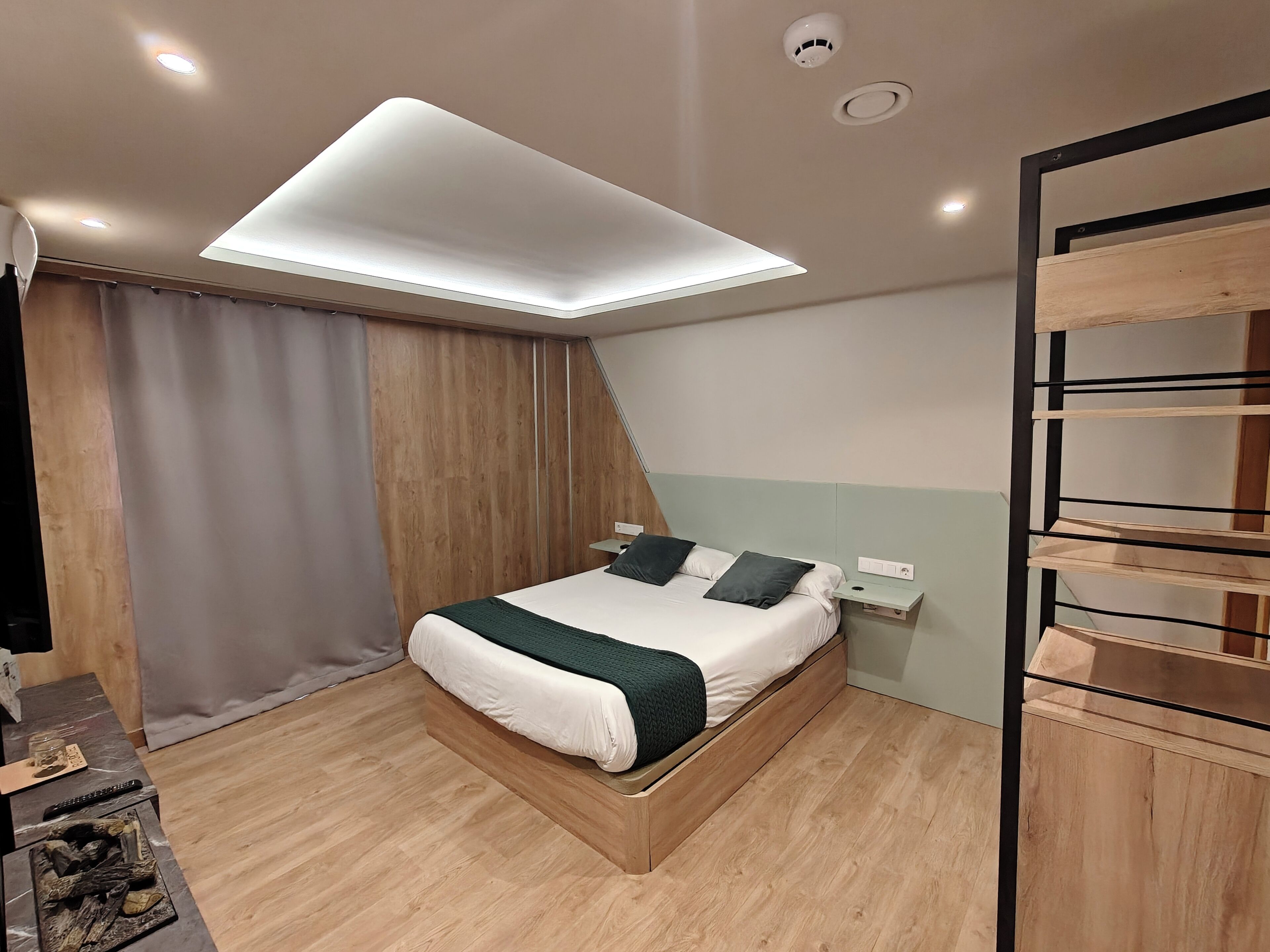 Ein modernes Schlafzimmer mit Bett, Nachttisch, Wandregal und Deckenleuchte.