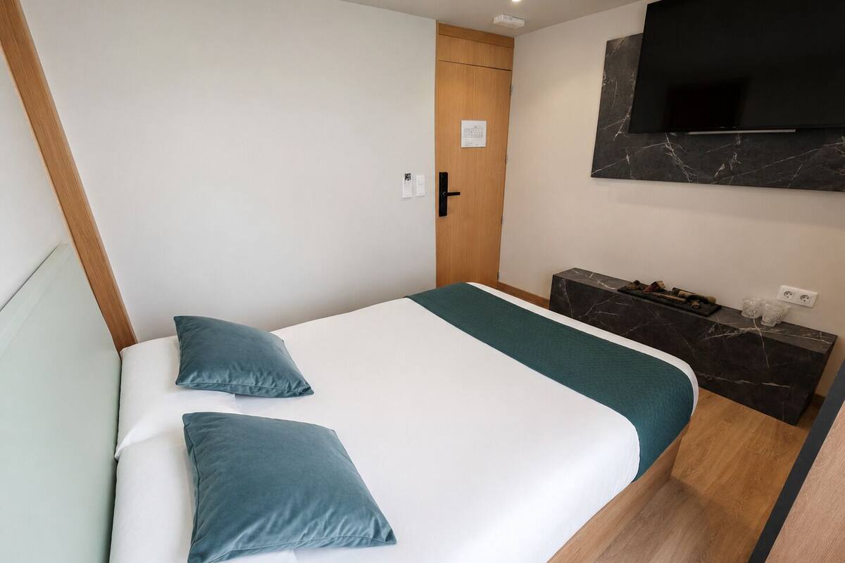 Un dormitorio con cama, dos almohadas, un televisor y una mesita con encimera de mármol.