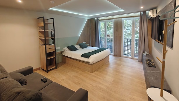 Un dormitorio moderno con cama, estanterías empotradas, televisor y balcón con cortinas.