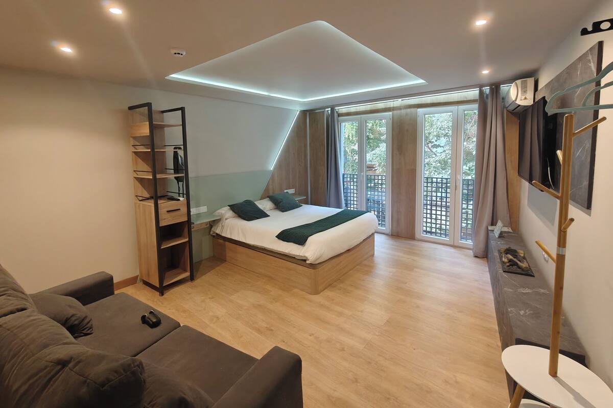 Un dormitorio moderno con cama, estanterías empotradas, televisor y balcón con cortinas.