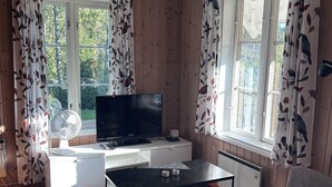 Olohuone, jossa on televisio, sohva ja ikkunat, joissa on verhot.