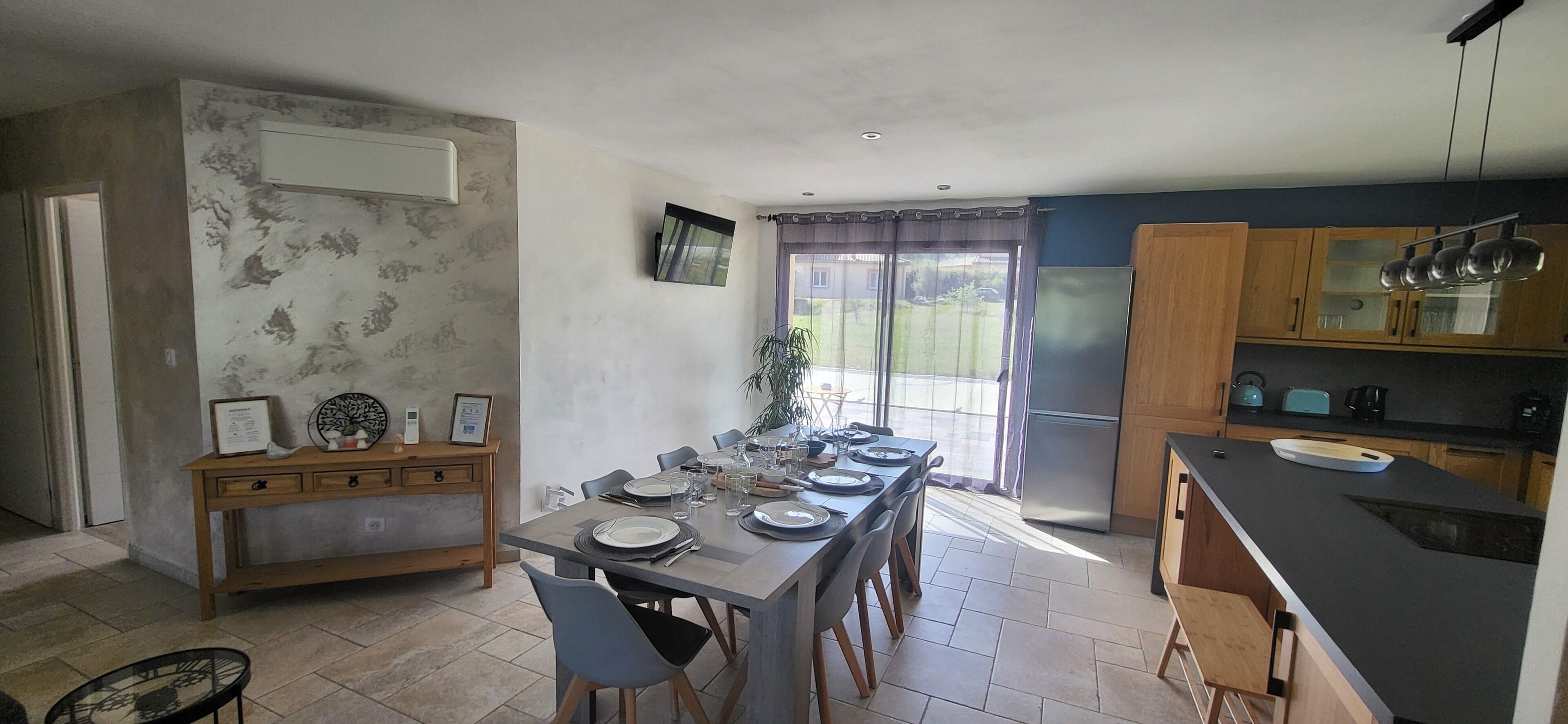 Cozinha com mesa de jantar posta para quatro pessoas, geladeira e armários de madeira.