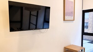 Ett modernt rum med en väggmonterad TV, en liten trähylla, en vit stol och en inramad tavla på väggen.