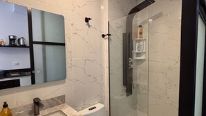 Ett modernt badrum med en dusch som är avskärmad med glasväggar, ett handfat i marmor och en toalett.