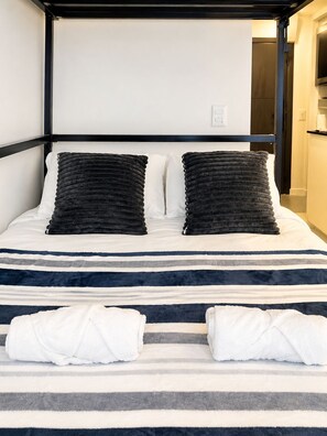 Ein Bett mit gestreifter Bettwäsche, zwei Kissen und zwei gefaltete Handtücher.