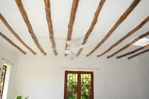 Una habitación con vigas de madera a la vista, un ventilador de techo y un ventanal con vistas a la vegetación.