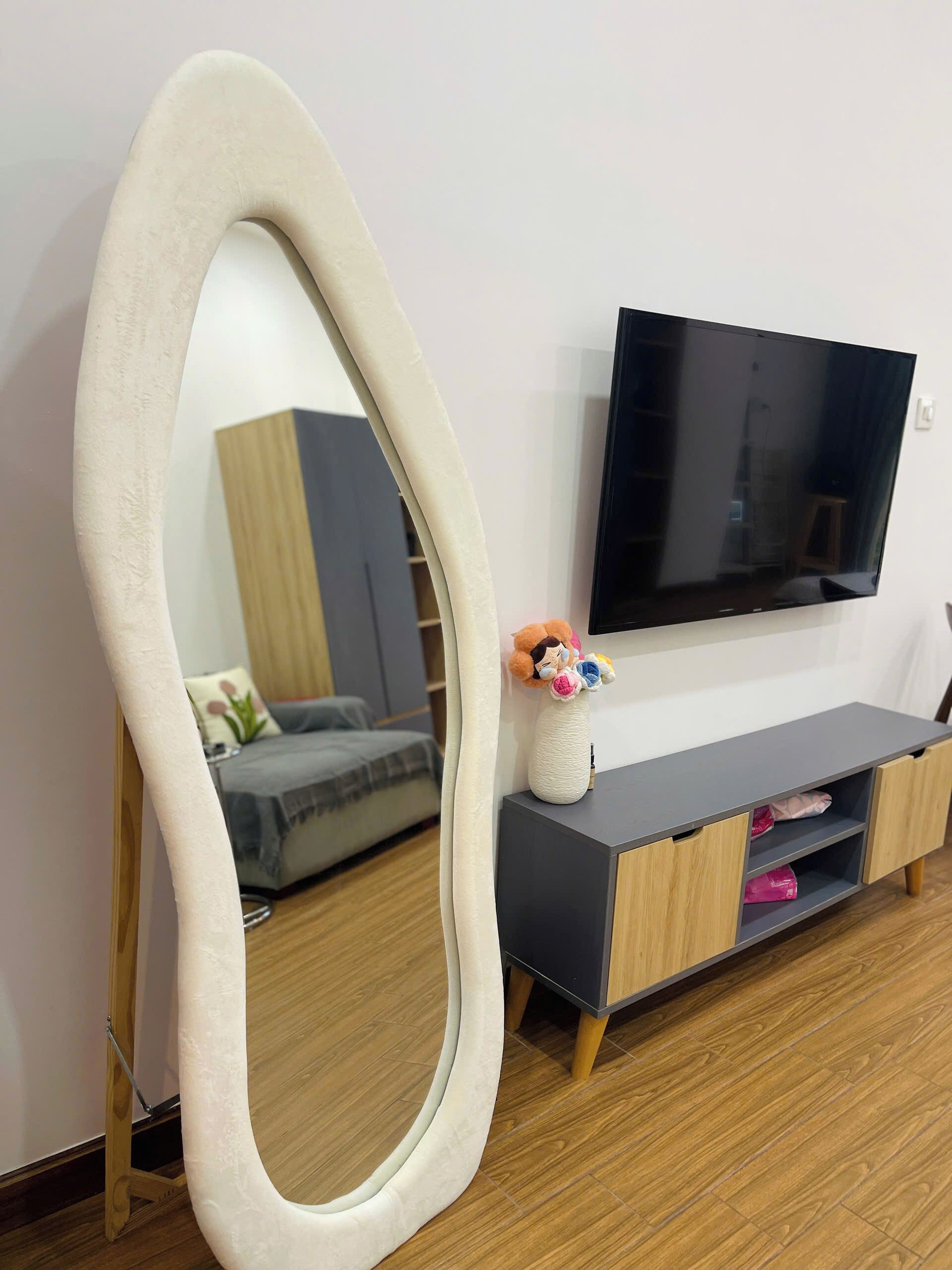 Ein modernes Wohnzimmer mit großem Spiegel, Flachbildfernseher, Sofa und Holzschrank.