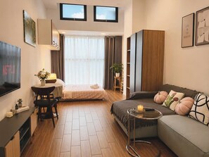 Moderni hotellihuone, jossa on sänky, sohva, televisio ja pieni pöytä, jonka päällä on kynttilä.