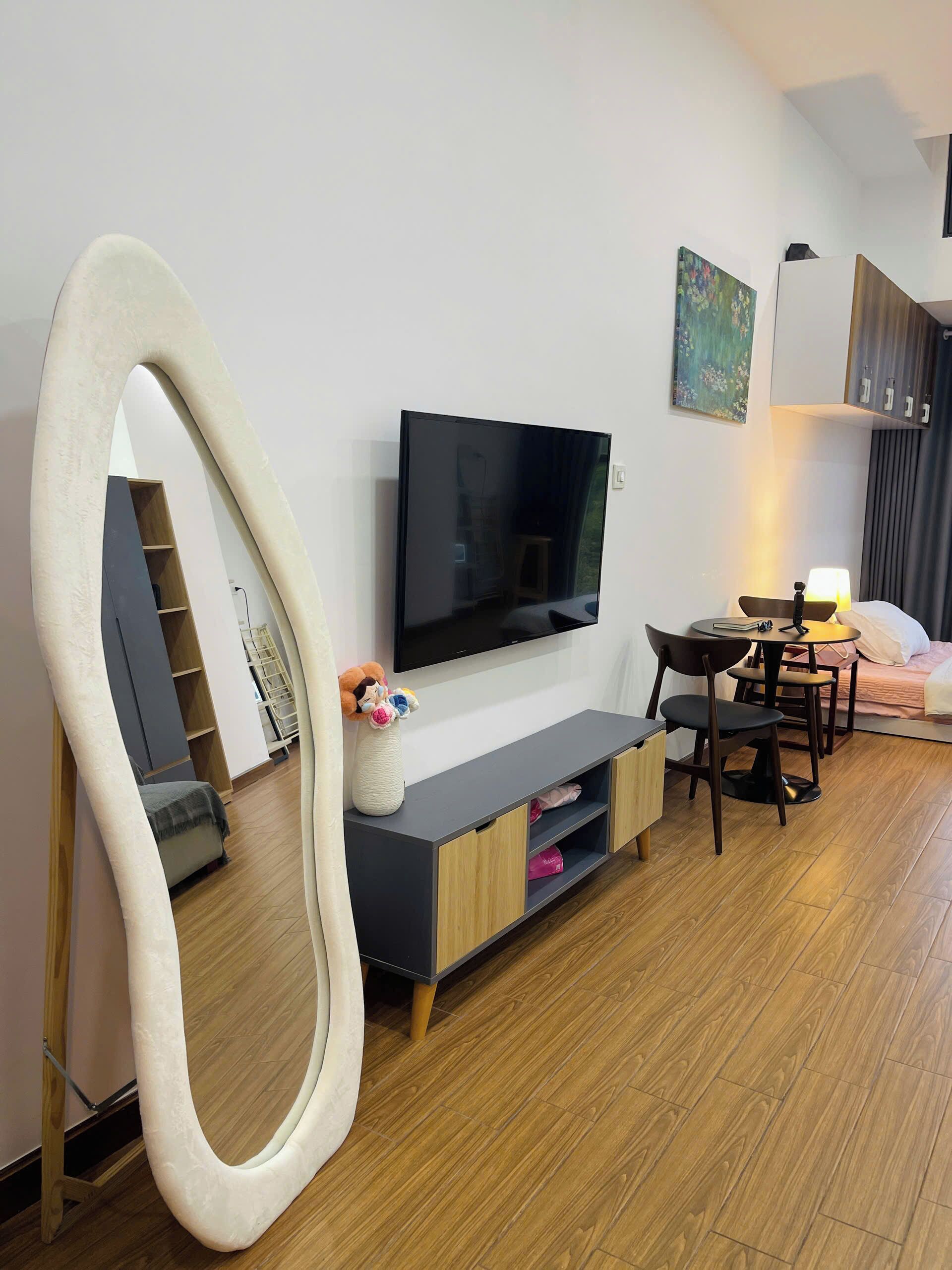 A modern living room with a flat-screen TV, a sofa, a dining area with a table and chairs, and a large mirror.