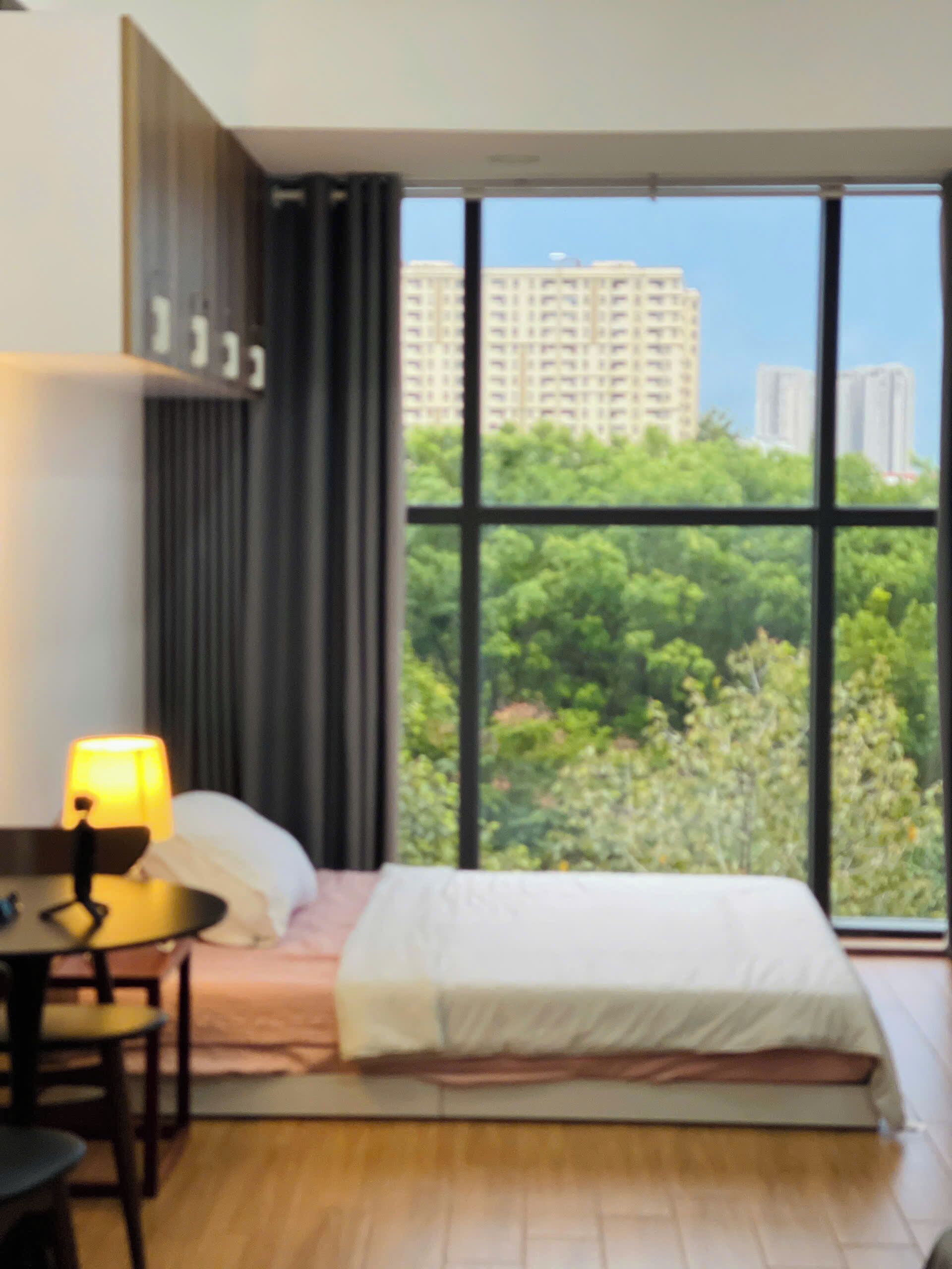 Una habitación de hotel con cama, escritorio, lámpara y un amplio ventanal con vistas a la ciudad.