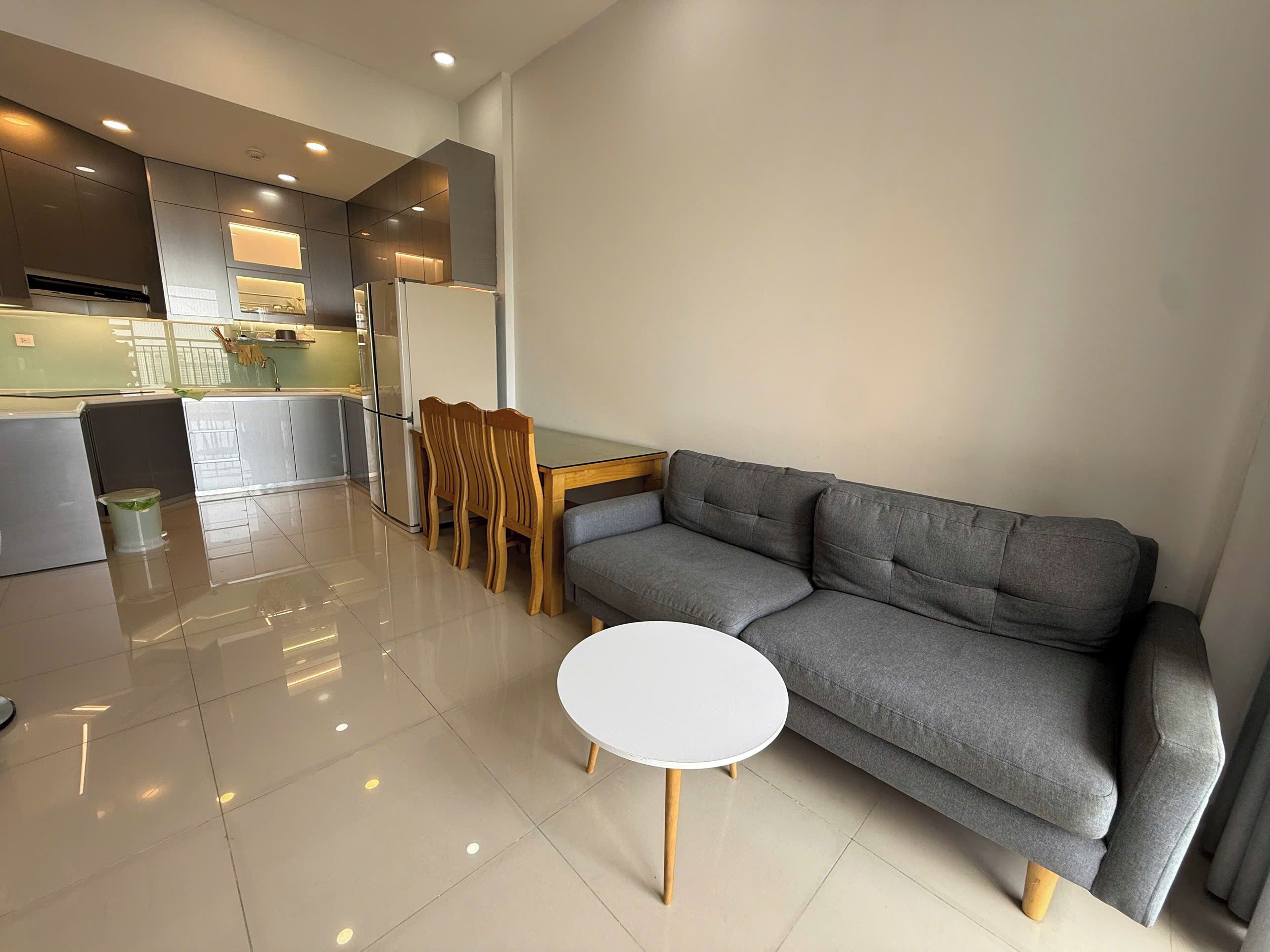 Un salon moderne avec un canapé gris, une petite table blanche et un coin repas avec des chaises en bois.