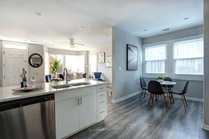 A modern kitchen with a built-in dishwasher, a dining area with a round table and chairs, and a ceiling fan. - The Garden @ Hunter’s Knoll | Walk to Forsyth Park (Savannah)
