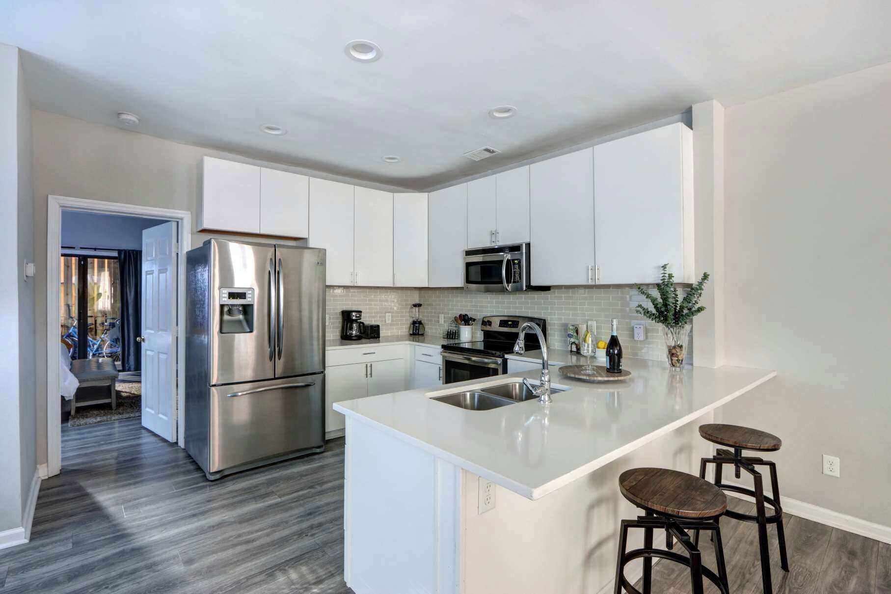 A modern kitchen with stainless steel appliances, a central island with bar stools, and a view into the adjacent living area.