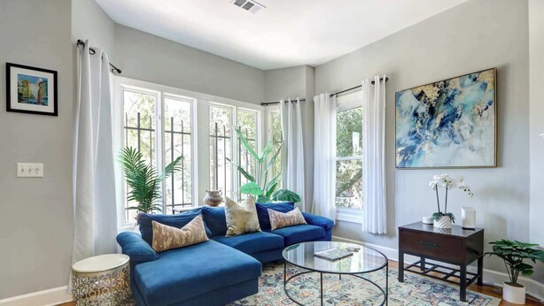 Ein modernes Wohnzimmer mit einem blauen Ecksofa, einem Glastisch und einem gemusterten Teppich.