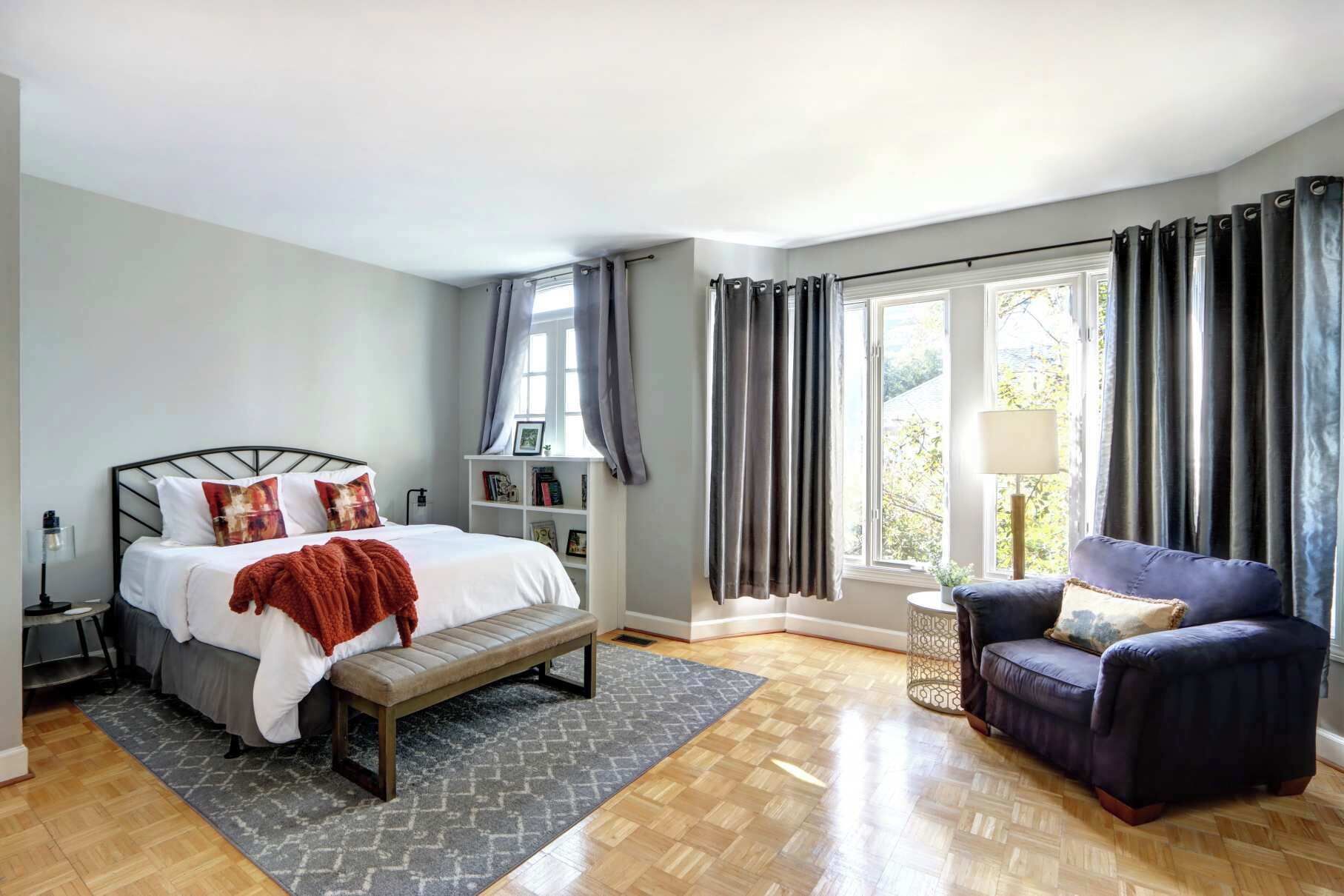 Un dormitorio con cama, banca, silla y ventana con cortinas.