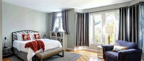 Un dormitorio con cama, banca, silla y ventana con cortinas.