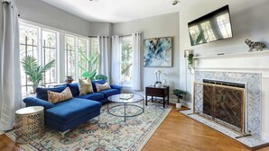 Ein geräumiges Wohnzimmer mit einem blauen Sofa, einem Kamin und großen Fenstern.