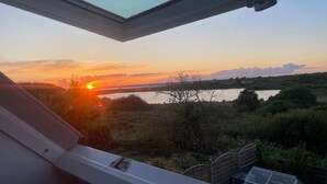 A view through a window with a metal frame, overlooking a natural landscape with a body of water and vegetation. - Breton interlude between sea and nature, terrace overlooking the pond (Ploemeur)