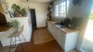 A kitchen with white cabinets, a wooden countertop, a sink, and a window. There are potted plants and a chair. - Breton interlude between sea and nature, terrace overlooking the pond (Ploemeur)