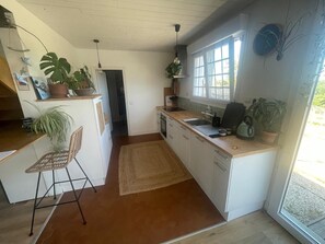 Eine Küche mit weißen Schränken, einer Holz Arbeitsplatte, einem Spülbecken und einem Fenster. Es befinden sich Blumentöpfe und ein Stuhl dort.