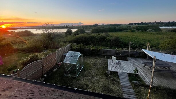 A view of a sunset over a grassy area with a wooden deck and a greenhouse. - Breton interlude between sea and nature, terrace overlooking the pond (Ploemeur)