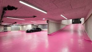 Un parking au sol recouvert d’un revêtement et aux murs de couleur rose, avec une voiture noire et des piliers en béton.