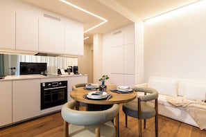A modern kitchen with a dining area, white cabinetry, and a wooden dining table with chairs.