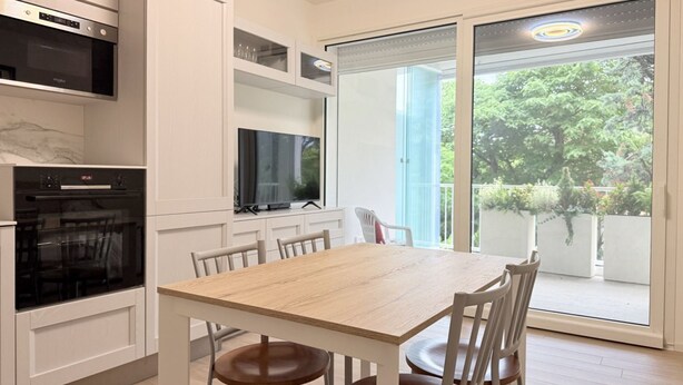 A modern kitchen with built-in appliances, a dining table with chairs, and a sliding glass door leading to a balcony with greenery. - SE276 - Senigallia, elegant apartment with a/c close to all main services (Senigallia)