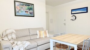 A living room with a sofa, a wooden dining table, and chairs. There is a framed picture on the wall and a clock. - SE276 - Senigallia, elegant apartment with a/c close to all main services (Senigallia)