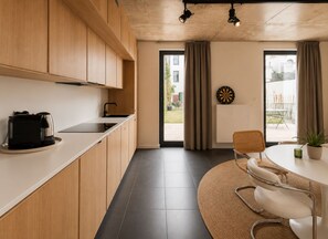 Eine moderne Küche mit Holzsärchen, einer Kaffeemaschine, einer Essecke mit rundem Tisch, Stühlen und einer Pflanze.