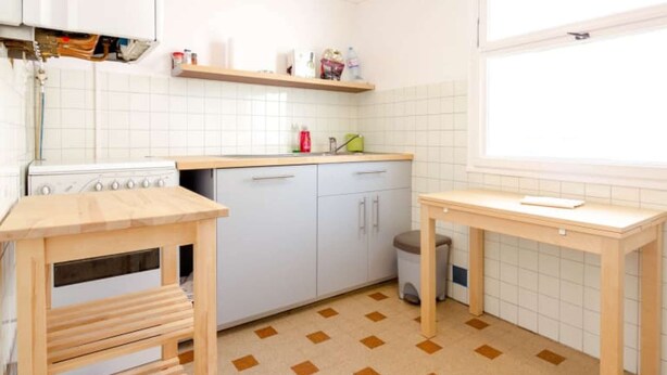 Een keuken met witte kastjes, een fornuis, een spoelbak en een raam.