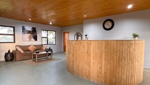 A spacious room with a wooden ceiling, a round wooden reception desk, a sofa, a coffee table, and a clock on the wall.