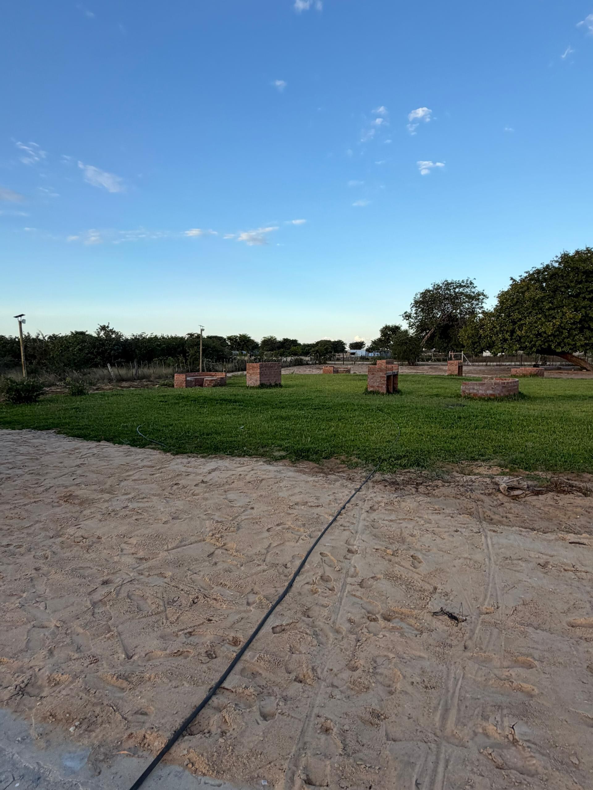 Una zona arenosa con un campo cubierto de césped, estructuras de ladrillo y árboles.