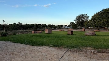 Una zona arenosa con un campo cubierto de césped, estructuras de ladrillo y árboles.