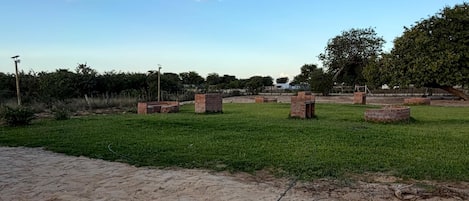 Una zona arenosa con un campo cubierto de césped, estructuras de ladrillo y árboles.