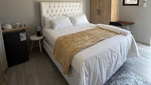 A bedroom with a bed, bedside tables, a wardrobe, a small desk, a lamp, and a rug.