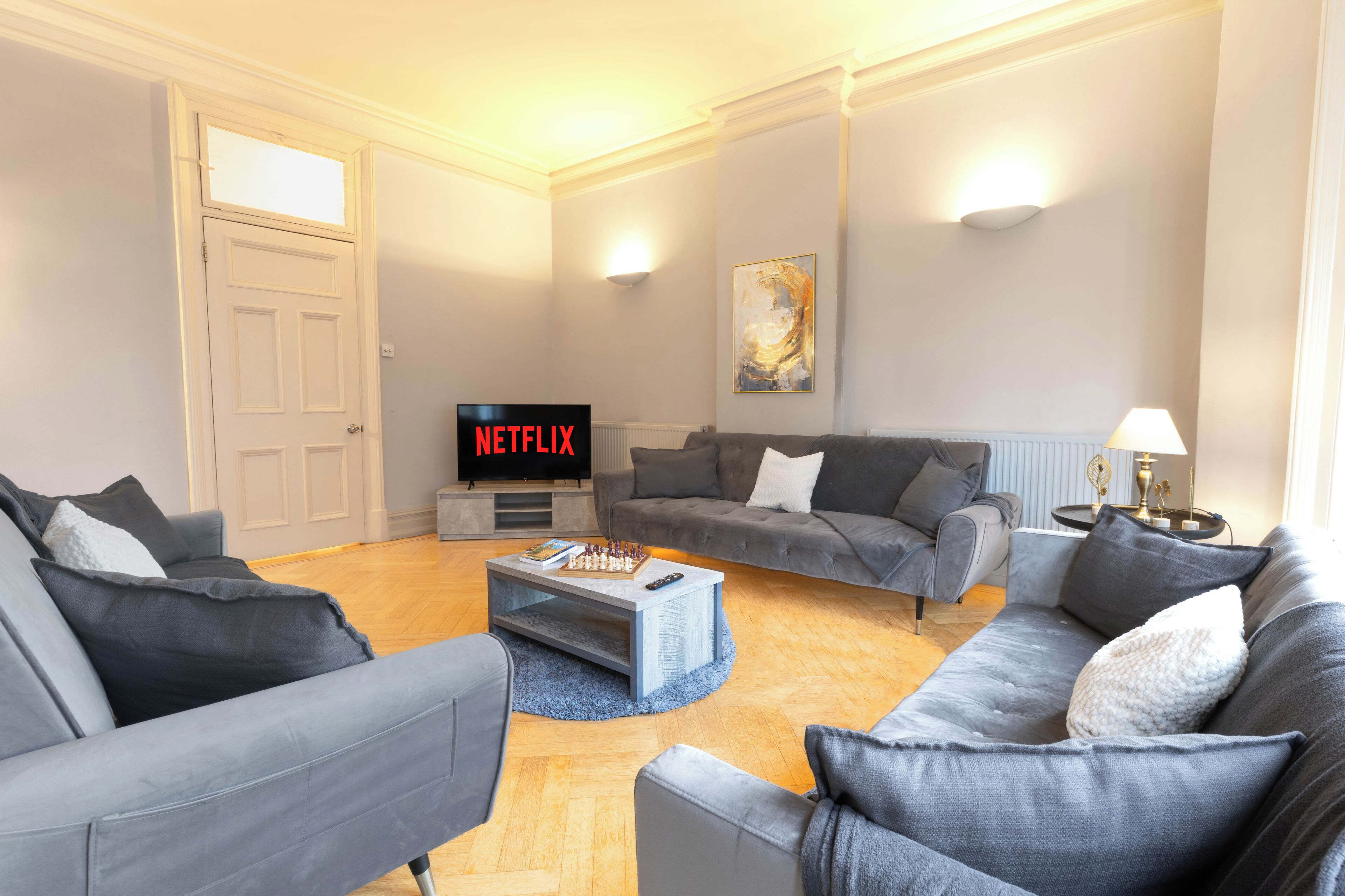 Un salon moderne avec des canapés gris, une table basse, un téléviseur à écran plat et un tableau accroché au mur.