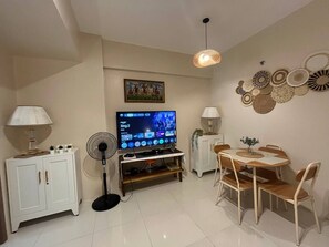 Ein Wohnzimmer mit Flachbildfernseher, Ventilator, Esstisch mit Stühlen und Wandbildern.