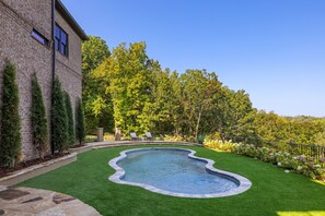 A swimming pool with a stone border, surrounded by a well-maintained lawn and a brick building. - Above Nashville Tranquility | Pool & Spa | 10 Acres | Gated (Nolensville)