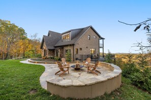 A house with a stone patio, outdoor seating, and a view of the surrounding landscape. - Above Nashville Tranquility | Pool & Spa | 10 Acres | Gated (Nolensville)