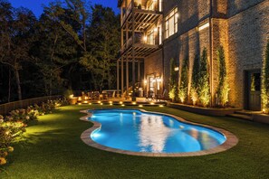 A swimming pool with a curved edge, surrounded by a well-manicured lawn and a brick building with multiple balconies. - Above Nashville Tranquility | Pool & Spa | 10 Acres | Gated (Nolensville)