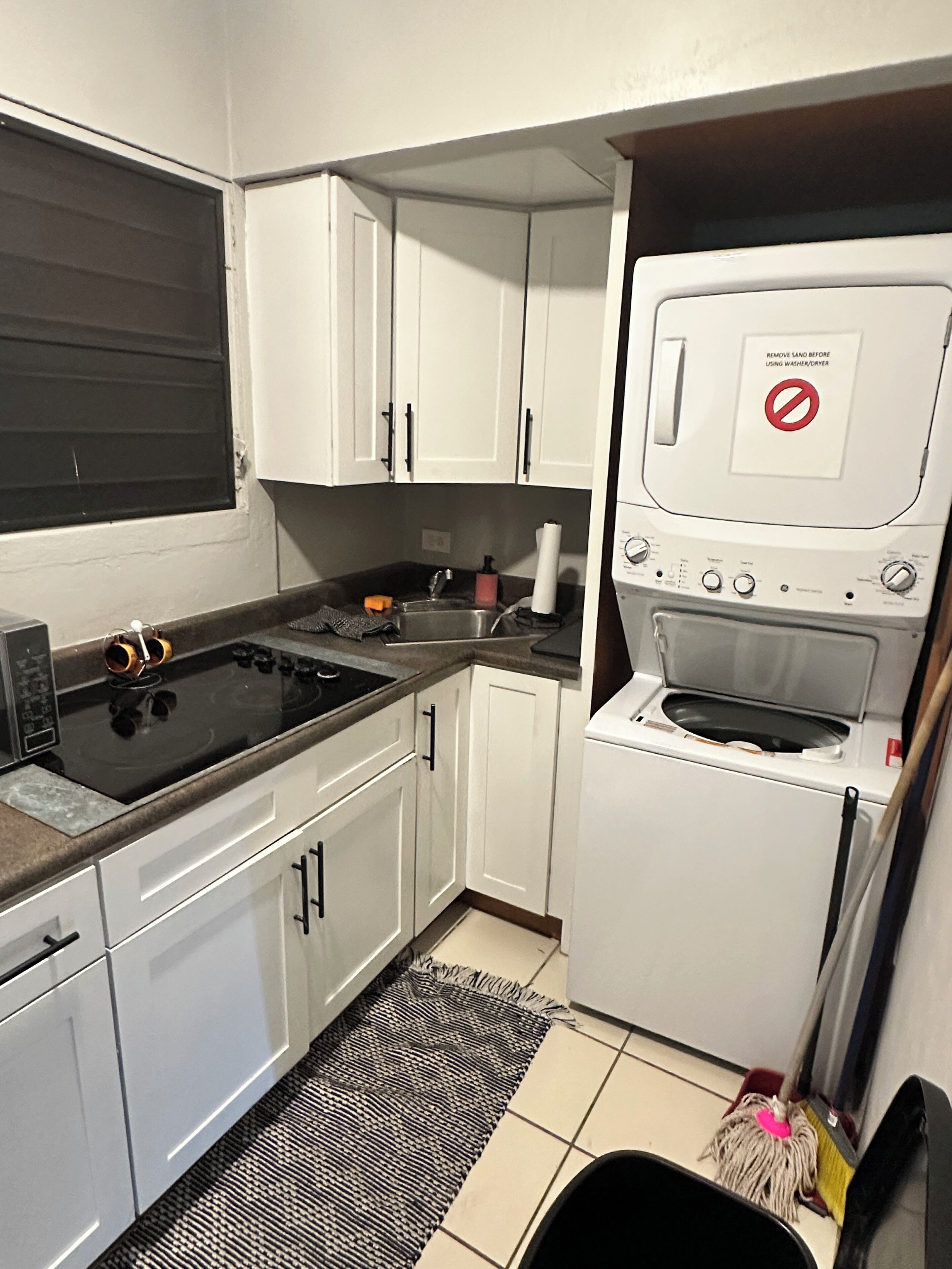 Una cucina compatta con mobili bianchi, un piano cottura nero, un forno integrato e un lavello.