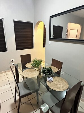 A dining area with a glass table, four chairs, and a potted plant. - 2-bedroom apartment in beautiful San Juan with AC (San Juan)