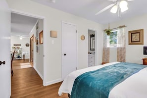 A bedroom with a bed, a ceiling fan, a window with curtains, and a door leading to a bathroom. - The Garden View / Near DFW Airport & AT&T stadium (Euless)
