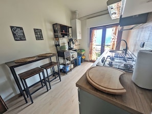 A kitchen with a gas stove, wooden stools, a coffee machine, and a view through the window. - The House of the Red Maple (Riva di Solto)