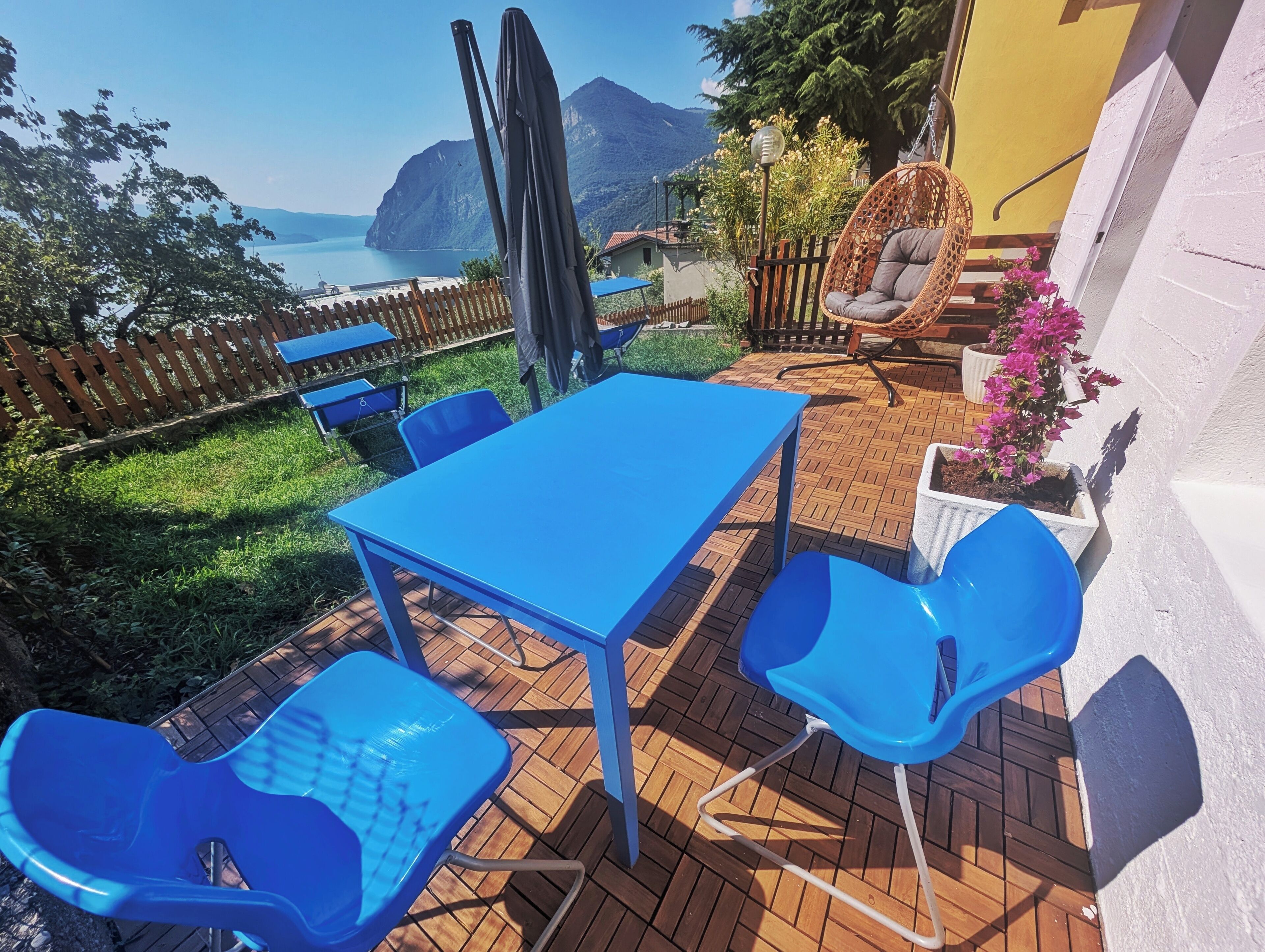 Une terrasse extérieure avec une table et des chaises, un fauteuil suspendu et une vue sur la mer et les montagnes.