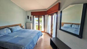 Un dormitorio con una cama grande, una mesita de noche, un espejo y una puerta corrediza de vidrio que da a un balcón.