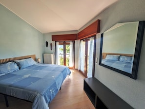 A bedroom with a large bed, a bedside table, a mirror, and a sliding glass door leading to a balcony. - The House of the Red Maple (Riva di Solto)