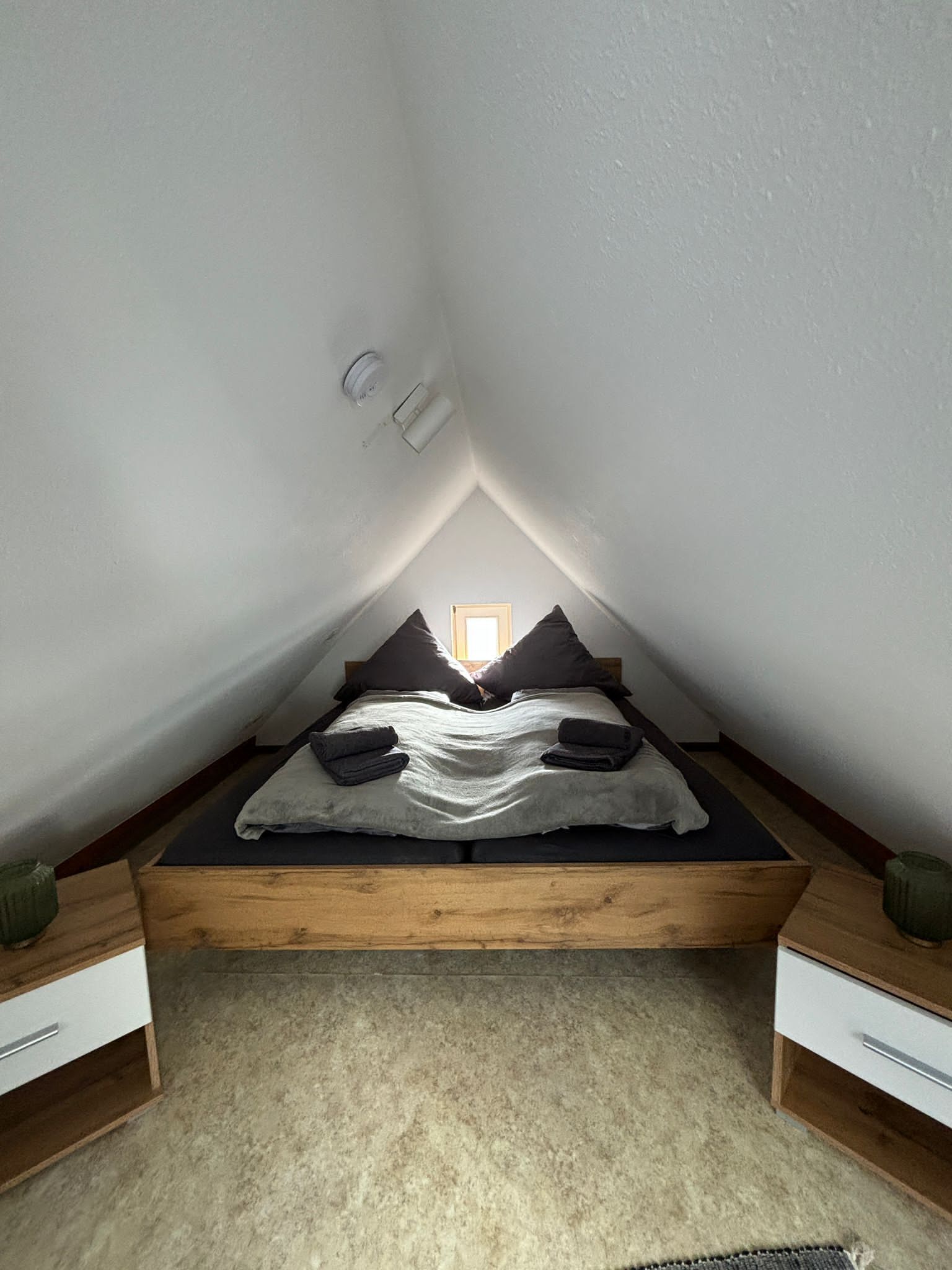 A small, sloped ceiling room with a bed, two nightstands, and a window.